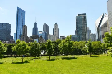Chicago skyline viewed from Grant Park with green grass and trees in the foreground.
