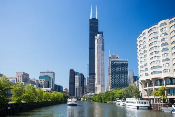 Willis Tower dominating the Chicago skyline with surrounding buildings and boats on the river.