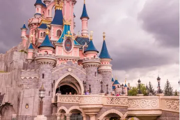 Sleeping Beauty Castle at Disneyland Paris with pink and blue turrets, golden accents, and a bridge with visitors.