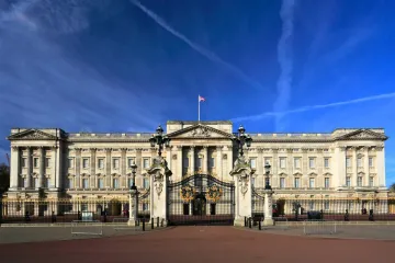 Front view of Buckingham Palace in London with a clear blue sky and the Union Jack flag flying.