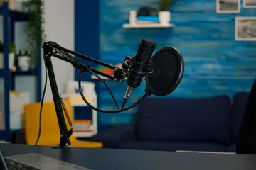 Professional condenser microphone and pop filter on a desk-mounted boom arm in a modern home podcasting setup.