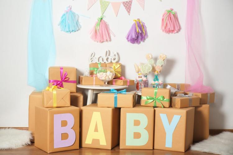 Pastel tassels, triangular flags and sheer fabric drapes. Brown paper-wrapped gift boxes with ribbons spelling baby in big pastel letters. Glass jars with candies on a small table.