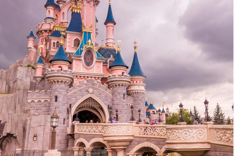 Sleeping Beauty Castle at Disneyland Paris with pink and blue turrets, golden accents, and a bridge with visitors.