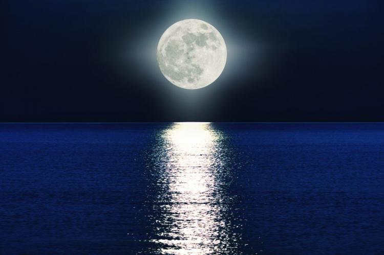 Full moon shining over a calm body of water, with the moonlight creating a reflective path on the water's surface against a dark night sky.