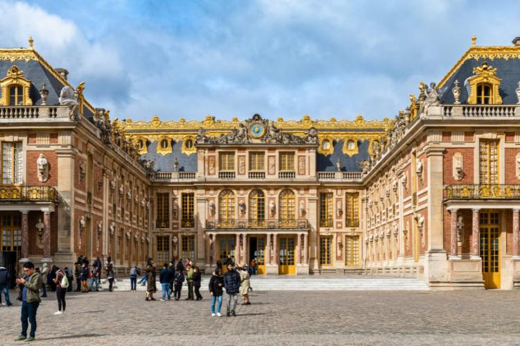 Main courtyard of the Palace of Versailles with golden accents and tourists.
