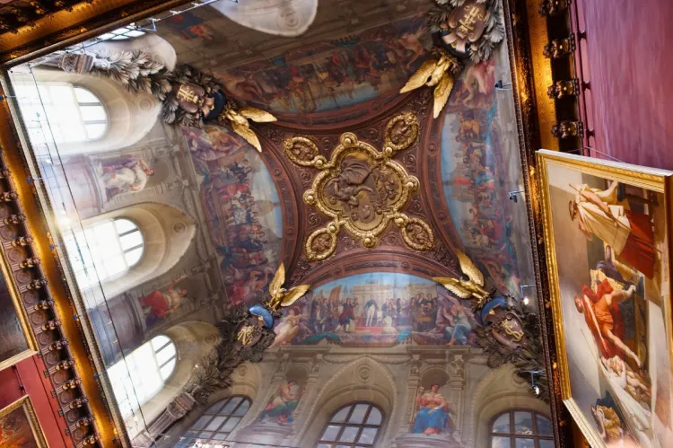 Ornate ceiling paintings at the Louvre Museum featuring golden details and mythological scenes.