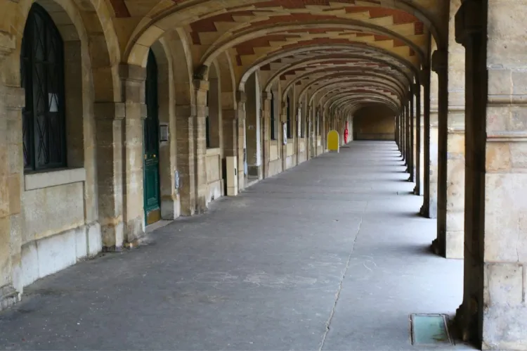 Long arched Victor Hugo corridor, in the street where the writer lived, with stone columns, red and beige tiled ceiling, and a green door, creating a sense of depth in a historic building.