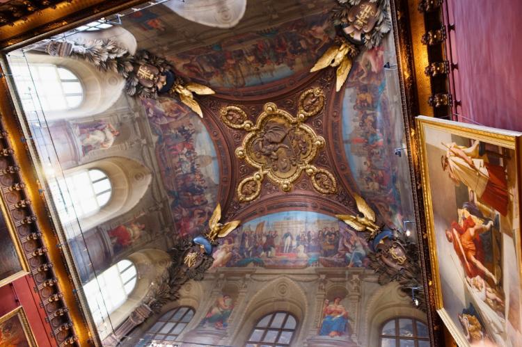 Ornate ceiling paintings at the Louvre Museum featuring golden details and mythological scenes.