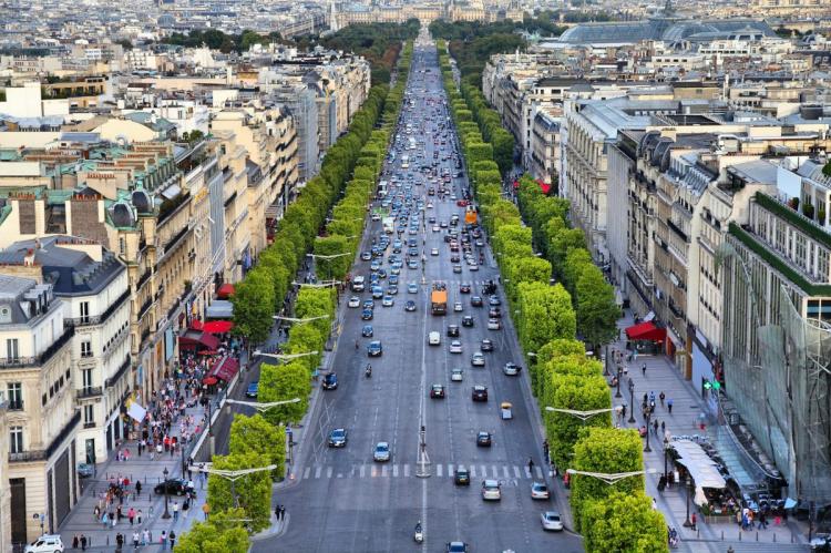 Elevated view of the Champs-Élysées in Paris, with bustling traffic, tree-lined sidewalks, and people enjoying the shops and cafes along the iconic boulevard.
