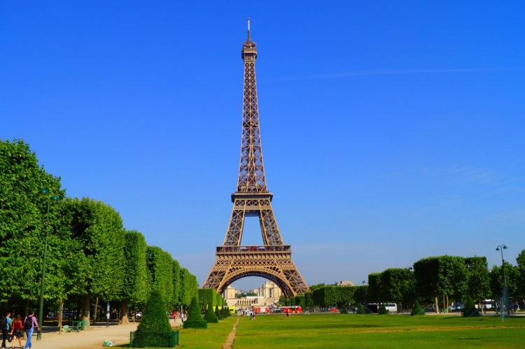 The Eiffel Tower in Paris on a clear day, surrounded by trees and a wide open space.