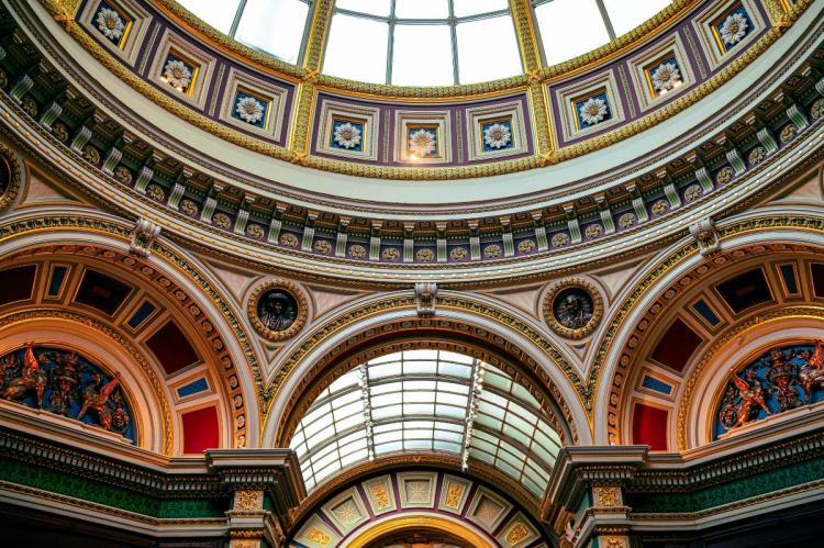 Ornate interior view of the London National Gallery dome with floral motifs, golden accents, and arched murals in a classical architectural style, illuminated by a skylight.
