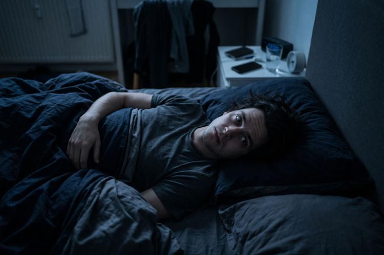 Person lying awake in bed at night, unable to sleep in a dark bedroom.