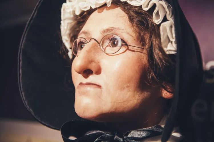Close-up of a wax figure of Madame Tussaud wearing round spectacles, a white bonnet and a black hood.