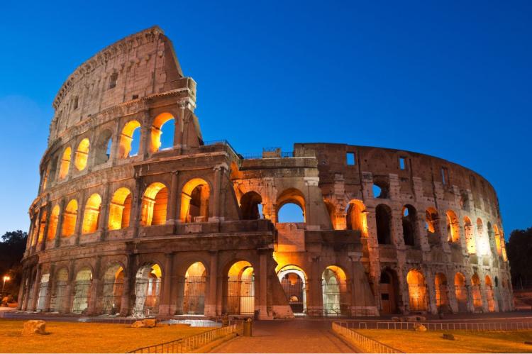 The Colosseum in Rome illuminated from within against a deep blue evening sky.