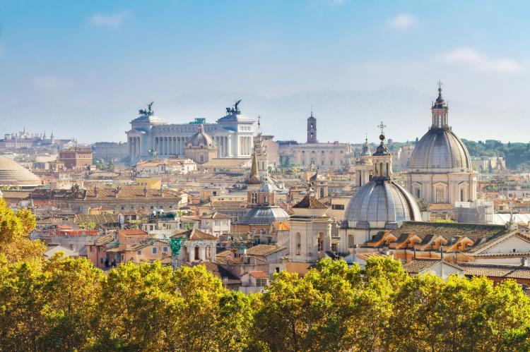 Panoramic view across the rooftops and domes of Rome under a bright blue sky.