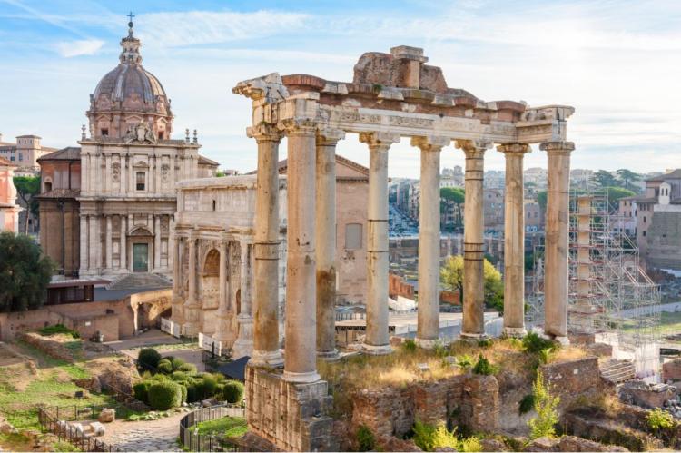 Ancient columns and ruins of the Roman Forum with historic buildings in the background in Rome.