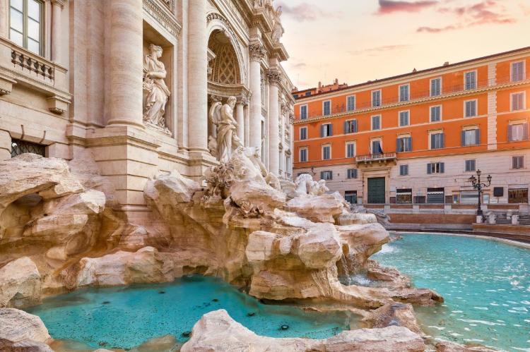Sculpted stone figures and turquoise water of the Trevi Fountain with buildings in the background.