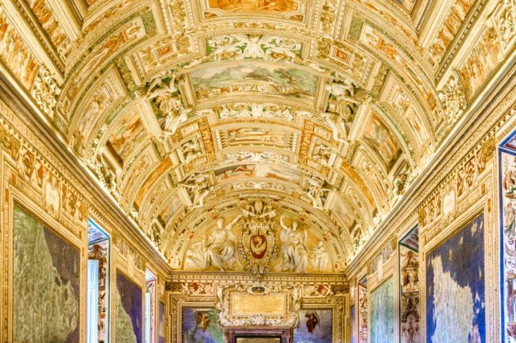 Ornately decorated vaulted ceiling with gilded details, paintings and frescoes in the Vatican Museums in Rome.