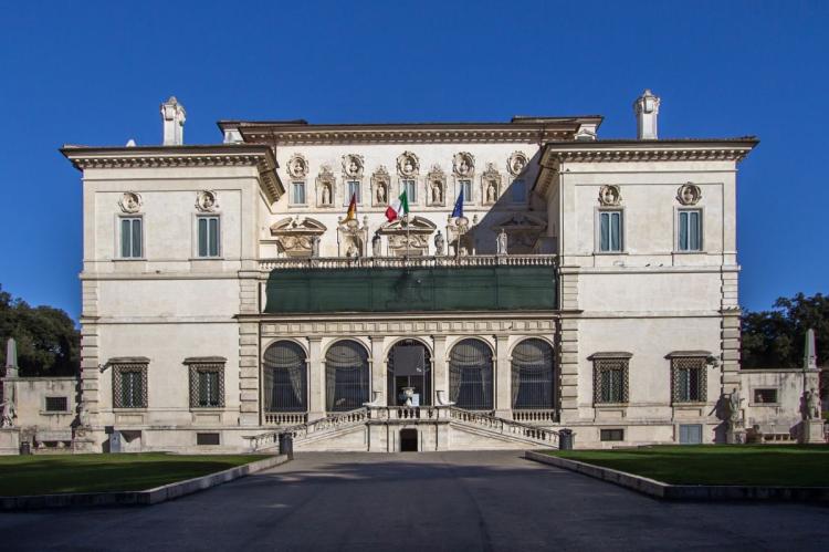 White façade of the Galleria Borghese with its arched entrance, statues and decorative architectural details.