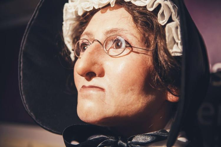 Close-up of a wax figure of Madame Tussaud wearing round spectacles, a white bonnet and a black hood.