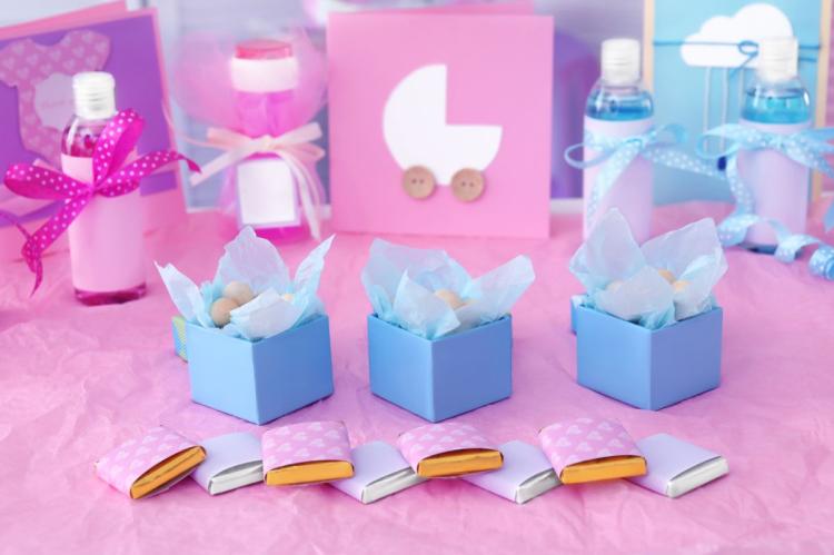Pink and blue baby shower favours with small gift boxes, ribbon-tied bottles and wrapped chocolates arranged on a decorated table.