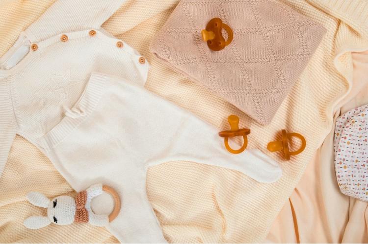 Knitted baby clothes, amber-coloured dummies and a soft bunny teething toy arranged as baby shower gifts.
