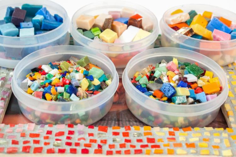 Assorted colorful mosaic tesserae sorted into five transparent plastic containers.