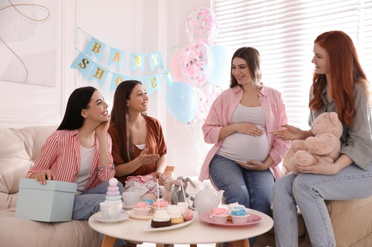 Pregnant woman celebrating with friends at a baby shower with balloons, cakes and gifts.
