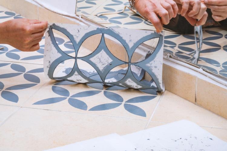 Decorative blue leaf pattern being stencilled onto cream floor tiles beside a mirror.
