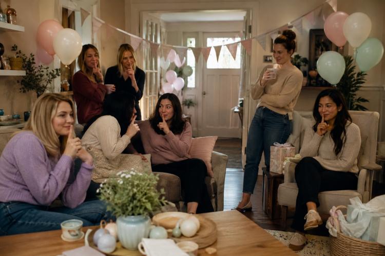 Guests waiting quietly in a decorated living room before a surprise baby shower begins.