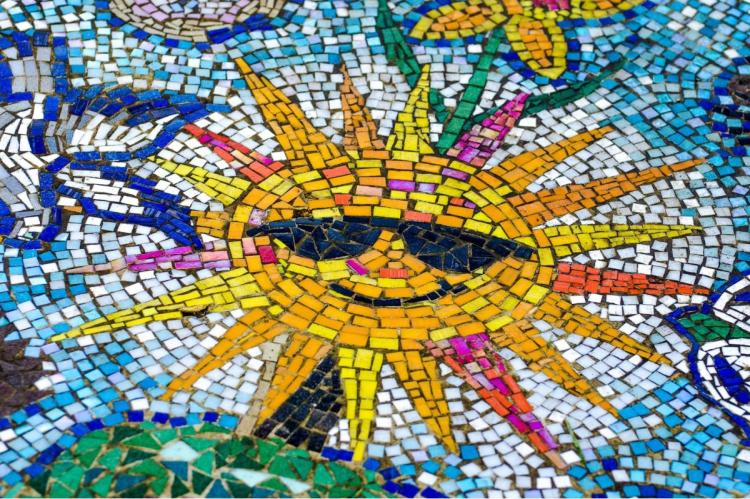 Colorful mosaic artwork depicting a stylized yellow sun surrounded by blue, white, and green tiles.