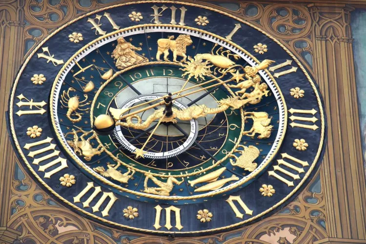 An ornate gilded astronomical clock on a painted Gothic façade, with a ring of zodiac signs and figures, black Gothic hour numerals, a golden sun-and-dragon hand and a month dial labelled in German.
